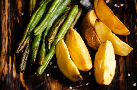 Baked potatoes and green beans are served on wooden platter. Eating at the restaurant. Vegetarian and vegan menu concept. Delicious vegetable food.の写真素材