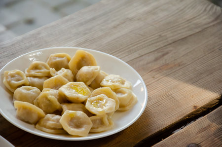 Plate with dumplings stands on wooden table. Rural still life. Homemade ravioli served in white platter on wooden surface with copy space. Delicious meal concept.の写真素材