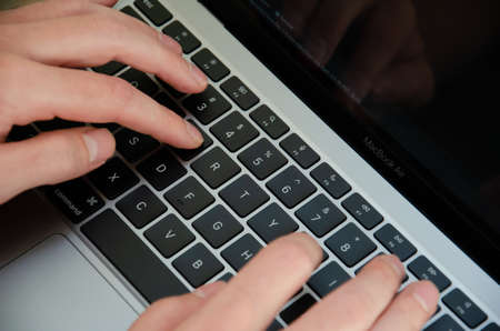 Kiev, Ukraine - September 5 2021. Caucasian man uses MacBook Air M1. Person is working on the latest Apple laptop. Top view hands on device keyboard.のeditorial素材