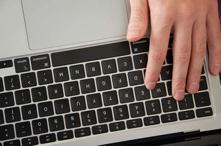 Caucasian man uses laptop. Person is working online on personal computer. Top view hands on device...