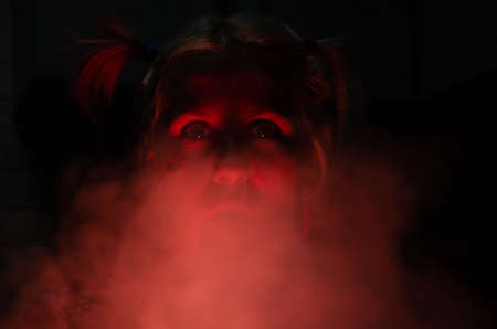 Crazy caucasian girl in red light with smoke and mad look. Halloween costume. Celebration concept.