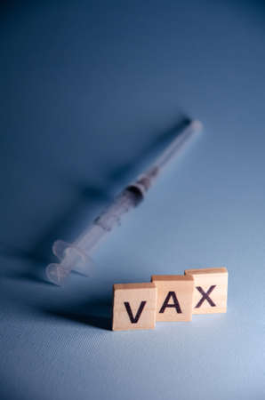 virus vaccination concept. Inscription Vax stands on blurred syringe background. Selective focus on Lettering Vax with copy space. Banner on blue background.の写真素材