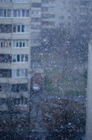 Snow falls on a blurred background of houses. Snowfall in the city. Winter weather. Background with snowflakes.の写真素材