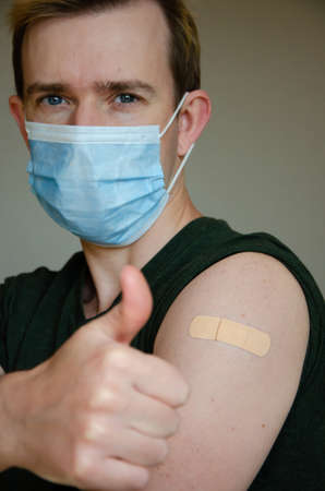 virus vaccination advertisement. Happy vaccinated man in medical mask shows hand with plaster after...