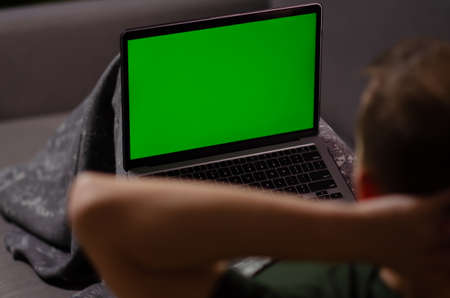 Caucasian man uses laptop with greenscreen of chromakey mockup. Person watches the video, relaxes,...