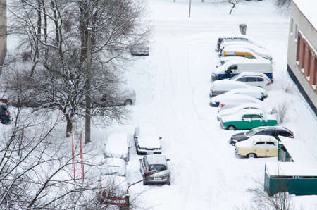 Cars are covered with snow. Winter weather in the city. The snowstorm covered the car park and the road between. Snow collapse.の写真素材