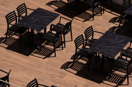 Tables and chairs on the terrace under the sun. Monochrome photo. Shadows from kitchen furniture....
