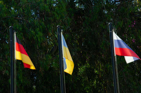 Ukrainian, Russian and German flags are waving in the wind on flagpoles. Political situation between Ukraine, Russia and Germany. The concept of international relations.の写真素材