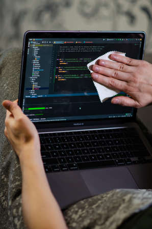 London, UK - January 12, 2022. Caucasian man wipes MacBook Air M1 screen with special napkin. Programmer is coding on latest Apple laptop. vertical footage.のeditorial素材