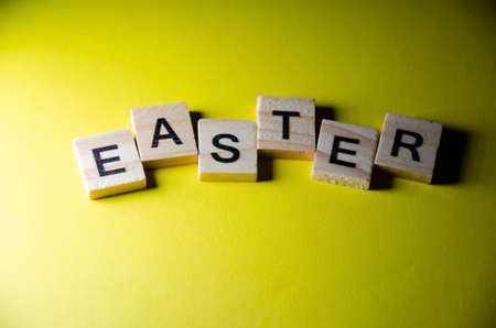 Inscription Easter outlined on yellow background with copy space. Selective focus on Lettering Easter made from wooden cubes. Celebration concept. Preparation for the holiday.の写真素材