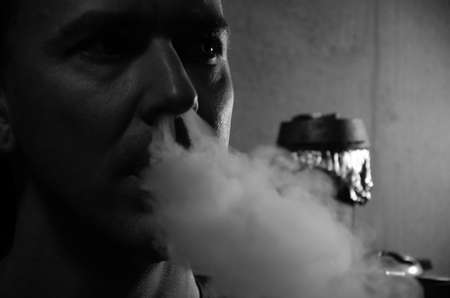 Caucasian man smokes hookah. Portrait of young man smoking shisha pipe and exhaling smoke. The...