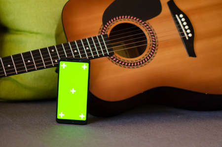 Selective focus on phone with greenscreen of chromakey mockup with tracking markers near the guitar...