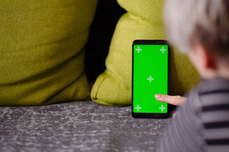 Green screen and chroma key. Caucasian woman holding mobile phone with greenscreen of chromakey mockup with tracking markers. Woman is resting at home and watching phone.の写真素材
