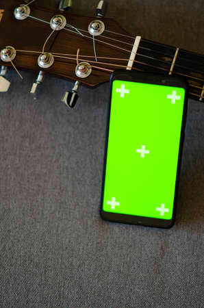 Selective focus on phone with greenscreen of chromakey mockup with tracking markers near the guitar...