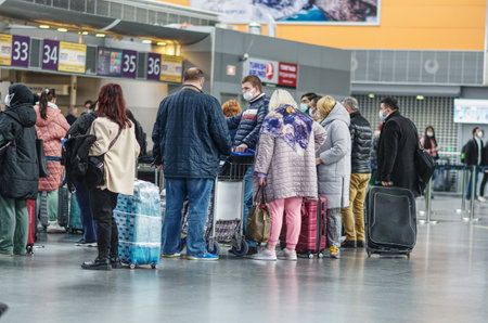 Group of travelers standing in queue at modern airport check-in area, wearing protective face masks...