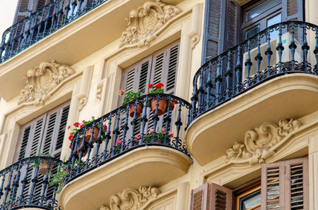 Picturesque balconies with iron railings and blooming flowers decorate a historic European apartment facade. Evokes a romantic urban atmosphere and architectural charm.の写真素材