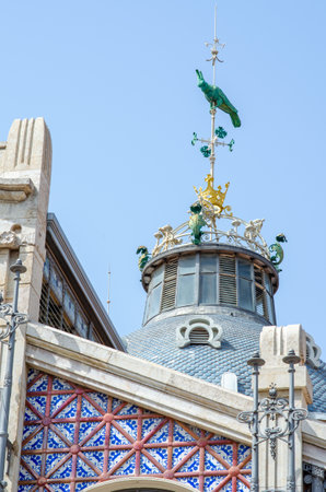 Art Nouveau architectural detail of the Central Market in Valencia, Spain, featuring ornate blue tiles, metalwork, and a decorative peacock sculpture on the roof.の写真素材
