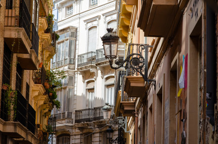 Charming narrow street in a European city adorned with vintage lamp posts and ornate balconies, showcasing beautiful sunlight on historic buildings and city life atmosphere.の写真素材