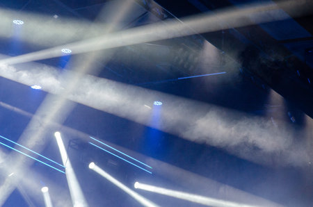 Dynamic beams of light and atmospheric fog create an energetic party mood in a concert venue,...
