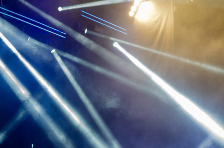 Dynamic beams of stage lights shining through smoke at a concert, creating a vibrant atmosphere....