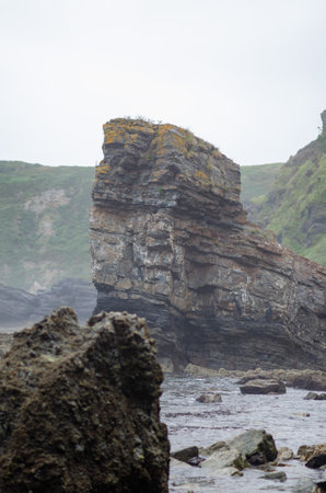Majestic sea stack stands tall on a rugged shoreline surrounded by misty cliffs and tidal rocks,...