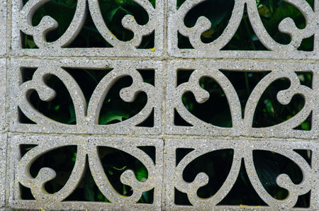 Closeup of a retro concrete block fence with elegant floral-inspired geometric cutouts and green foliage visible through the pattern, perfect for backgrounds or architectural concepts.の写真素材