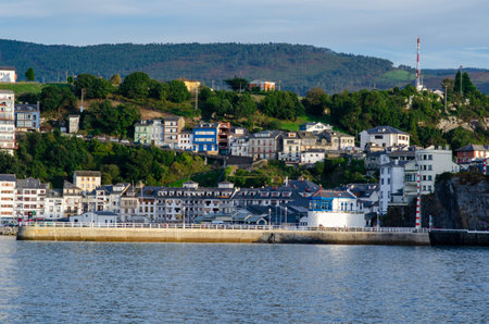 Scenic view of a vibrant coastal town with hillside houses overlooking the waterfront, green hills in the background, and tranquil sea in the foreground.の写真素材