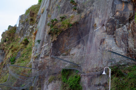 Protective metal netting installed on rocky mountain slope to prevent landslides and rockfalls, promoting safety in outdoor environments and infrastructure.の写真素材