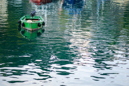 Small green boat drifts alone on a peaceful harbor with gentle water reflections, providing a tranquil and relaxing maritime scene for travel or nature concepts.の写真素材
