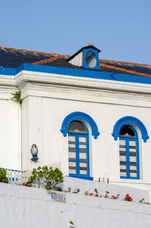 Traditional Mediterranean building facade with bright blue arched windows, vivid white walls, small garden and clear sky. Ideal for architecture, travel, and summer themes.の写真素材