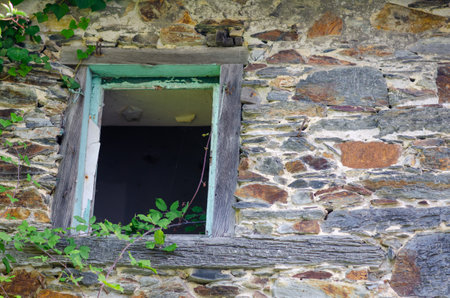 Close-up of a weathered stone wall featuring a vintage wooden-framed window partially covered by...