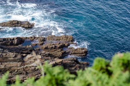 Scenic rocky shoreline with turquoise sea waves crashing against the cliffs, viewed from above with...