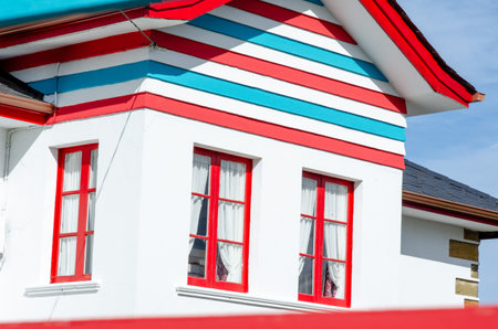 Bright modern house facade featuring vivid red-framed windows and bold horizontal stripes in blue, red, and white, evoking a cheerful coastal vibe.の写真素材