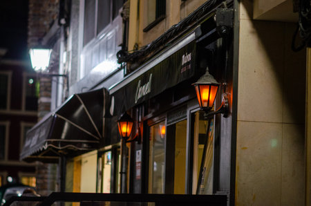 Urban nightlife scene featuring a warmly lit restaurant exterior and vintage wall lanterns, creating a cozy and inviting street atmosphere in the evening.の写真素材