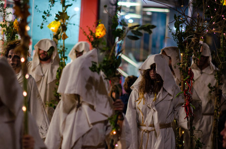 Participants dressed in white robes celebrate a traditional Spanish Halloween carnival at night, creating a mystical and atmospheric scene with foliage and lights.の写真素材