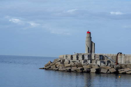 Modern concrete pier with a red lighthouse stands on the tranquil coastline, symbolizing navigation and safety at the harbor entrance. Coastal architecture concept.の写真素材