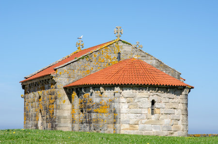 Historic stone chapel with traditional red roof sits on grassy hill, featuring ornate crosses and showing weathered textures, symbolizing heritage and tranquility.の写真素材