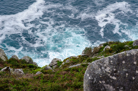 Dramatic top view of ocean waves hitting rugged rocks and green cliff, showcasing natural beauty and...