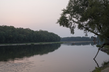 Wide river flowing across green forest. Fall. Evening. Reflections of trees in the calm water. Sundownの写真素材