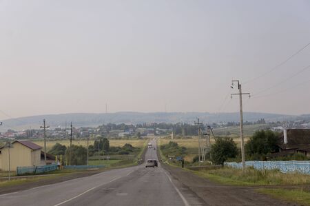 Sverdlovsk region, Ural, Russia. September 1, 2017. Asphalt road with cars on it going through mountains and green forests. Trees and their shadows on the grass. Sunny summer day with blue skyのeditorial素材