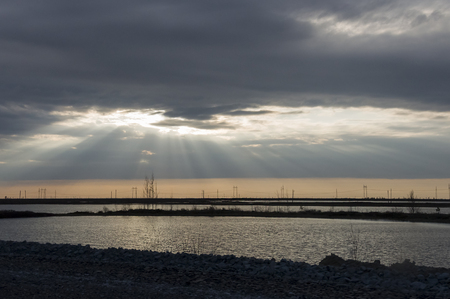 Late at night. Sundown and sunrises. River running through the field with reflections in the water. Evening with dark blue, violets colors in the sky. Silhouettes of dry grass and electric poles.の写真素材