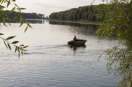 Fisherman are swiming on the boat. Wide river flowing across green forest. Fall. Evening....