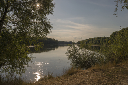 Wide river flowing across green forest. Fall. Morning reflections in the waterの写真素材