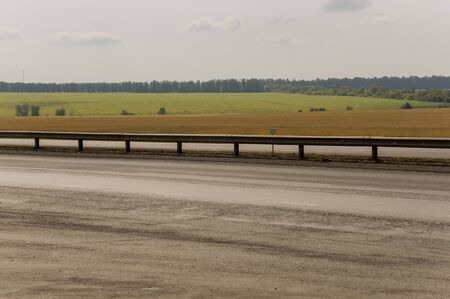 Big autumn field with trees in the blue sky. Asphalt road. Cars are riding. Traveling across Russia...