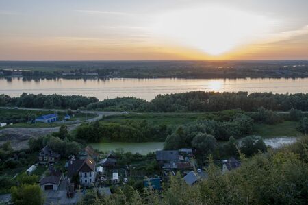 Small town with tiny houses near the river and green forests and fields. Trees and their shadows on...