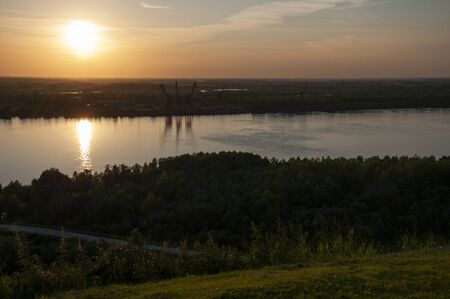 Small town with tiny houses near the river and green forests and fields. Trees and their shadows on the grass. Sundown and sunrises. View from high on the landscapeの写真素材