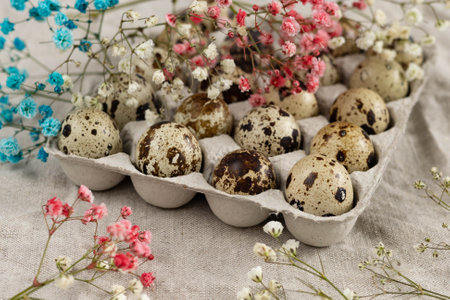 Quail eggs in a carton on a linen tablecloth with flowers