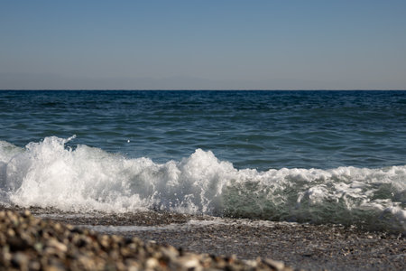 Sea waves on the pebble beach on a background of blue sky.の写真素材
