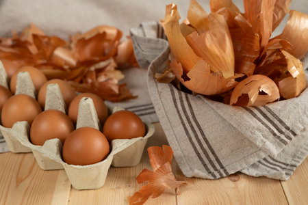 Eggs in a cardboard box on a wooden table with a yellow dry onion husk for coloring eggs, the concept of "Happy Easter."の写真素材