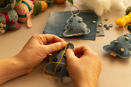 Female hands sews a felt Christmas tree on a light background.